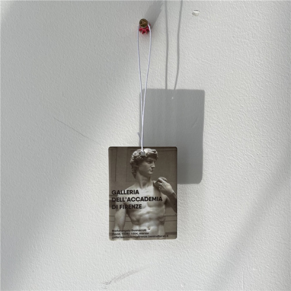 Clear acrylic keychain printed with a museum-ticket design, hanging against a white wall