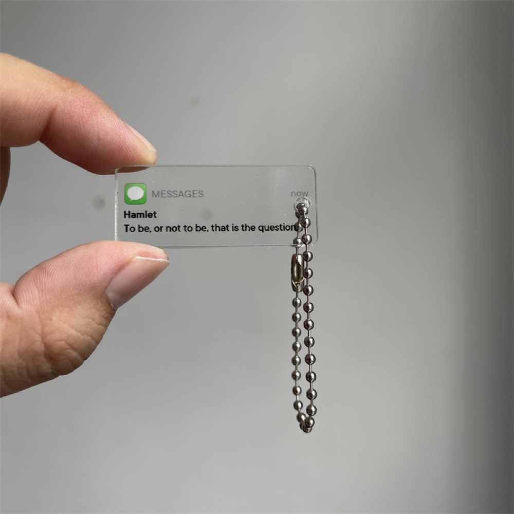 Fingers holding a small clear acrylic keychain with printed message artwork