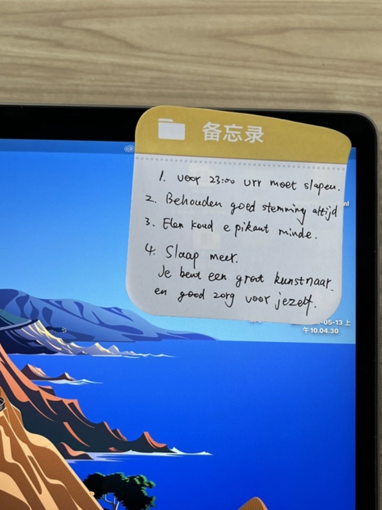 Sticky note with handwriting stuck to a laptop screen above a mountain wallpaper